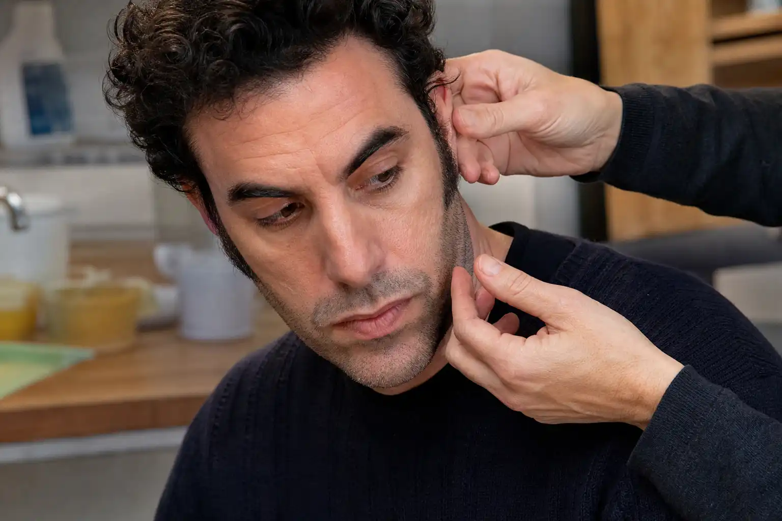 Des mains examinent un objet, autour de sacha baron cohen, dans une cuisine.